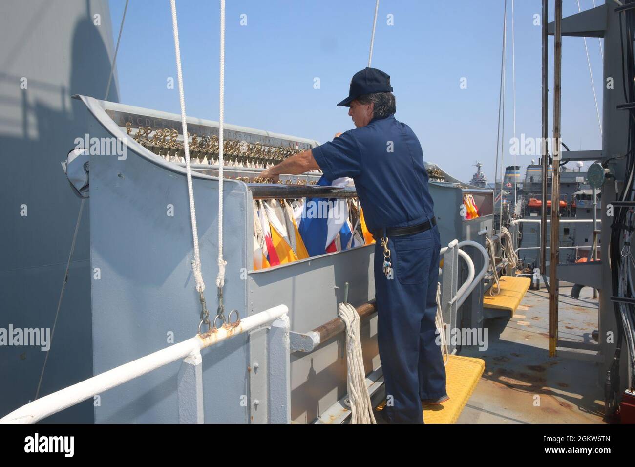 210707-N-AC165-0004 (July 7, 2021) – Larry James Gonzales, Sr., ordinary seamen aboard USNS Walter S. Diehl (T-AO 193), simulates using the flag signaling method to communicate. During specific underway evolutions such as underway replenishments, transiting areas such as the Straits of Hormuz, and during training events, Military Sealift Command vessels are expected to set various levels of Emission Control (EMCON) conditions, a status in which all fixed and or mobile radio stations in an area are asked to stop transmitting for safety or security reasons, said Captain Patrick Todd Christian, m Stock Photo