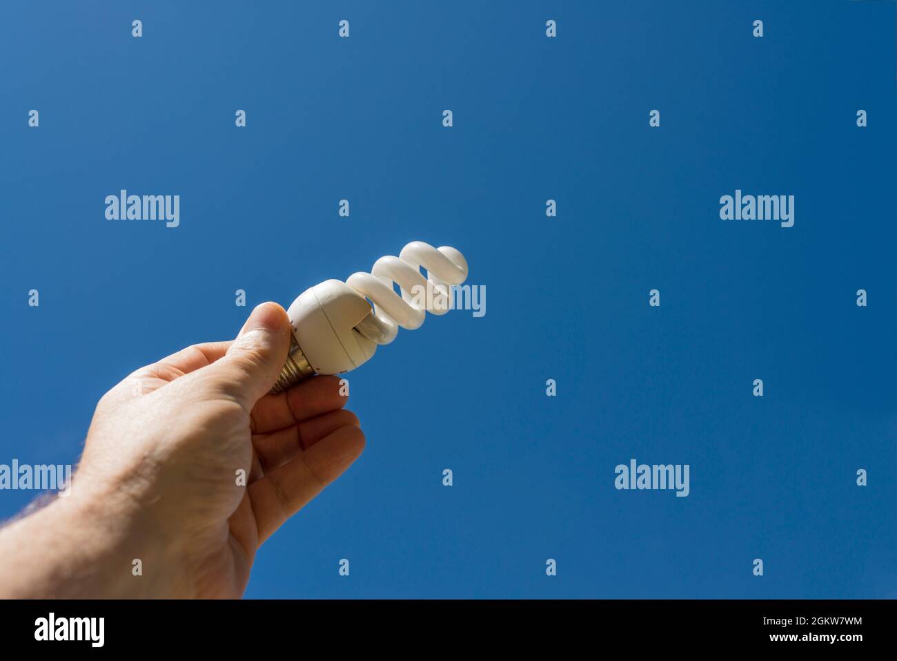 Hand holding a energy saving light bulb with a blue sky in the background. Clean energy concept. Stock Photo