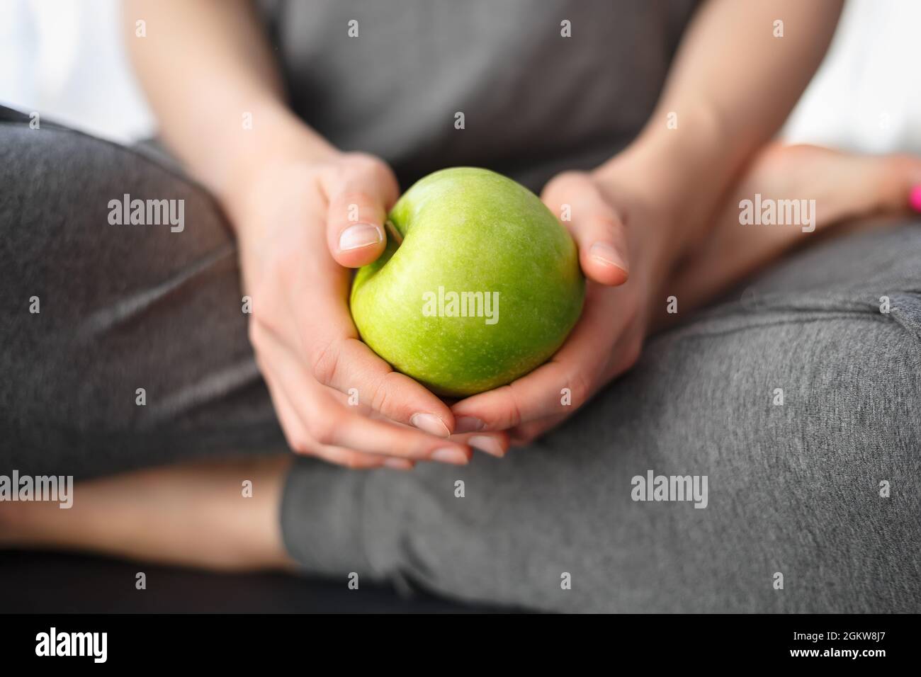 Young woman in grey sweat pants holding green apple for snack. Healthy eating and lifestyle concept. Eat low carbs vitamin fruits for health and weigh Stock Photo