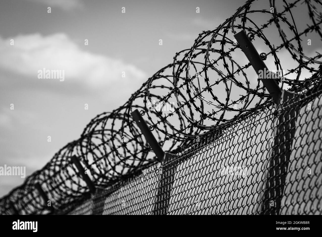 Barbed wire on top of metal mesh netting fence enclosing airport against cloudy sky Stock Photo