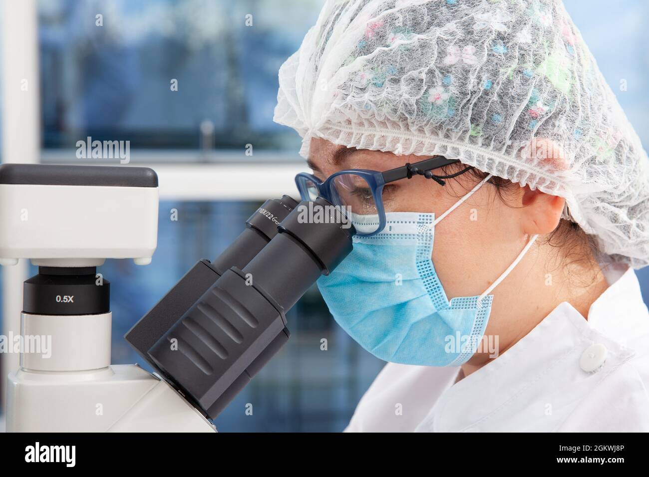 Young female scientist looking at samples under the microscope Stock Photo