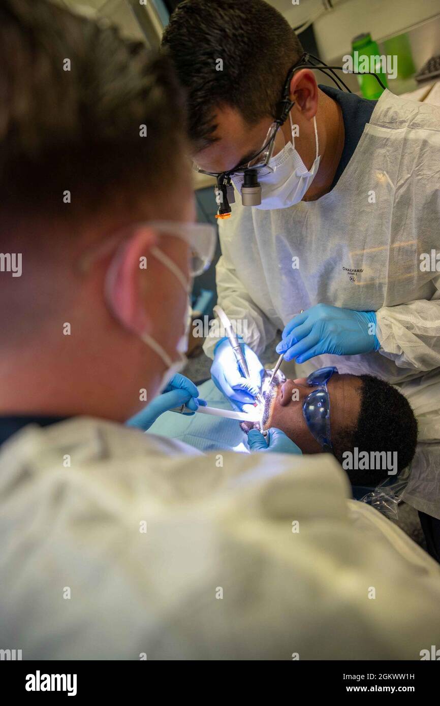 Aviation Boatswain's Mate (Handling) Airman Andrew Henderson, center, from New Lebanon, New York, assigned to USS Gerald R. Ford's (CVN 78) air department, undergoes a dental procedure from, Lt. David Anguiano, right, from Austin, Texas, and Hospital Corpsman 2nd Class Aaron Van Dike, from Mogadore, Ohio, assigned to Ford’s medical department, July 13, 2021. Ford is underway in the Atlantic Ocean conducting Full Ship Shock Trials. The U.S. Navy conducts shock trials of new ship designs using live explosives to confirm that our warships can continue to meet demanding mission requirements under Stock Photo