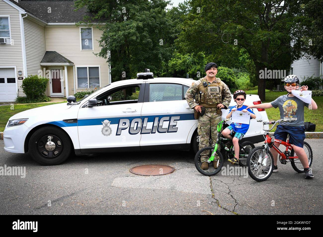 Senior Airman Carlos Howard, 66th Security Forces Squadron Positive Policing program lead, stands with Parker and Douglas Jones, Hanscom residents, after recognizing them with Blue Bucks for wearing proper safety gear while riding bikes at Hanscom Air Force Base, Mass., July 13. Blue Bucks are coupons to either a number of base restaurants, or Outdoor Recreation rentals. Stock Photo