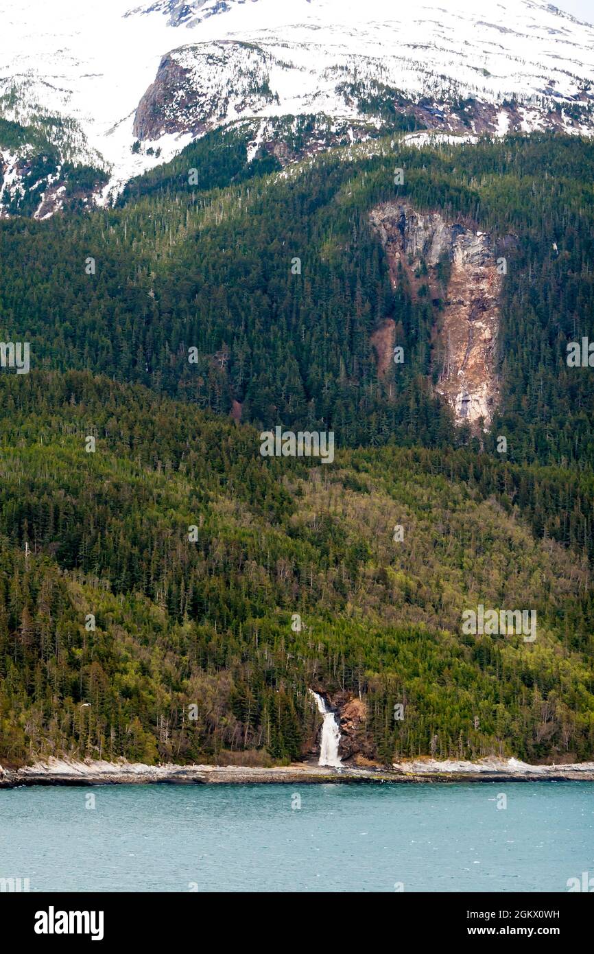 A waterfall flowing down a mountainside into the ocean along the Inside Passage, Alaska Stock Photo