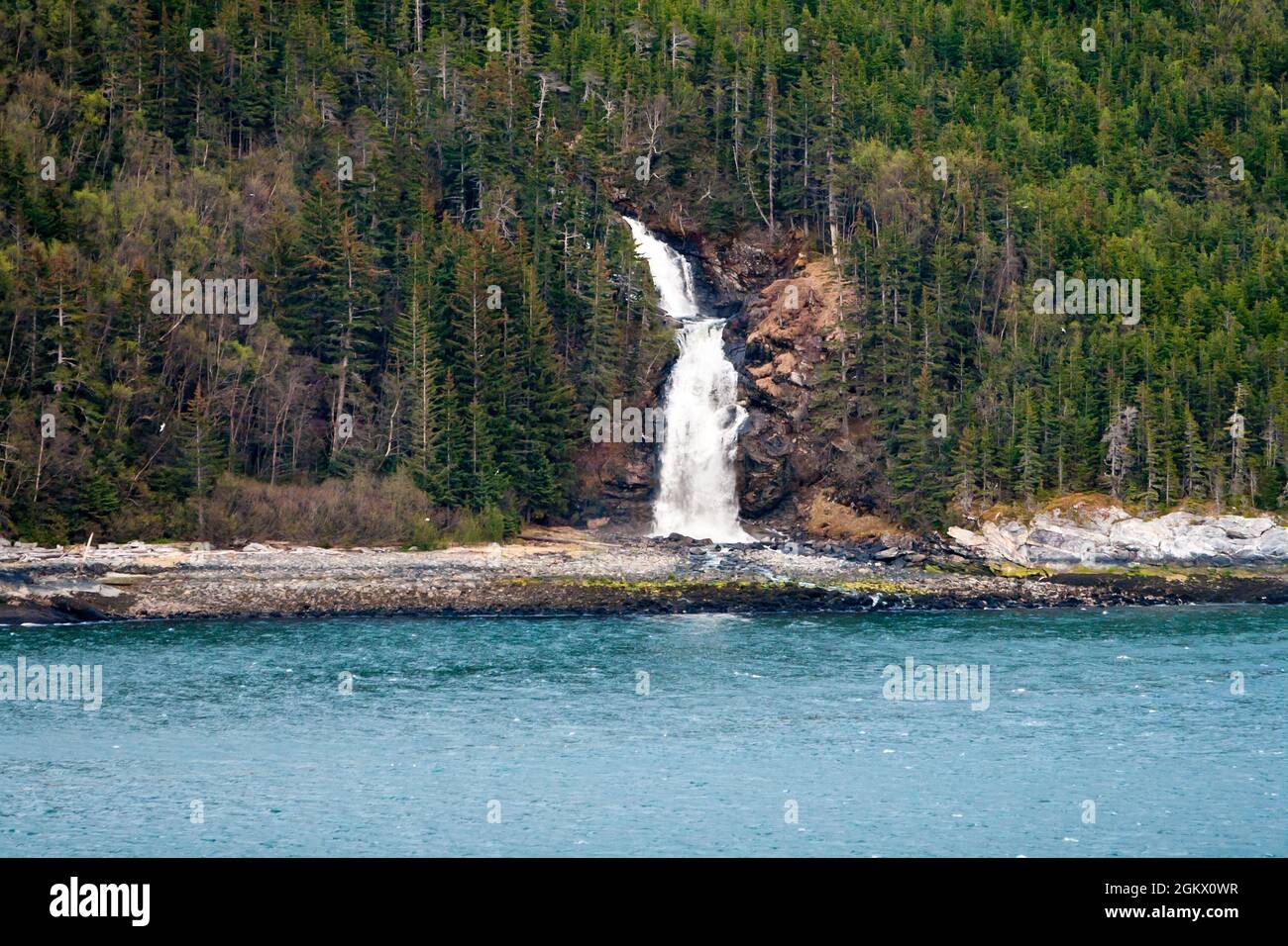 A waterfall flowing down a mountainside into the ocean along the Inside Passage, Alaska Stock Photo