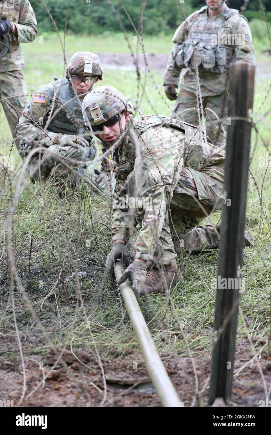 New York Army National Guard Spc. Joshua Klotzbach, assigned to Bravo Company, 152nd Brigade Engineer Battalion, emplaces a bangalore torpedo in a triple strand concertina wire obstacle during demolition training at Fort Drum, New York on July 14, 2021. The 152nd BEB's combat engineer companies practiced their mobility and counter-mobility mission during annual training using C4 explosives, shaping and cratering charges, bangalores, and explosively formed projectiles. Stock Photo