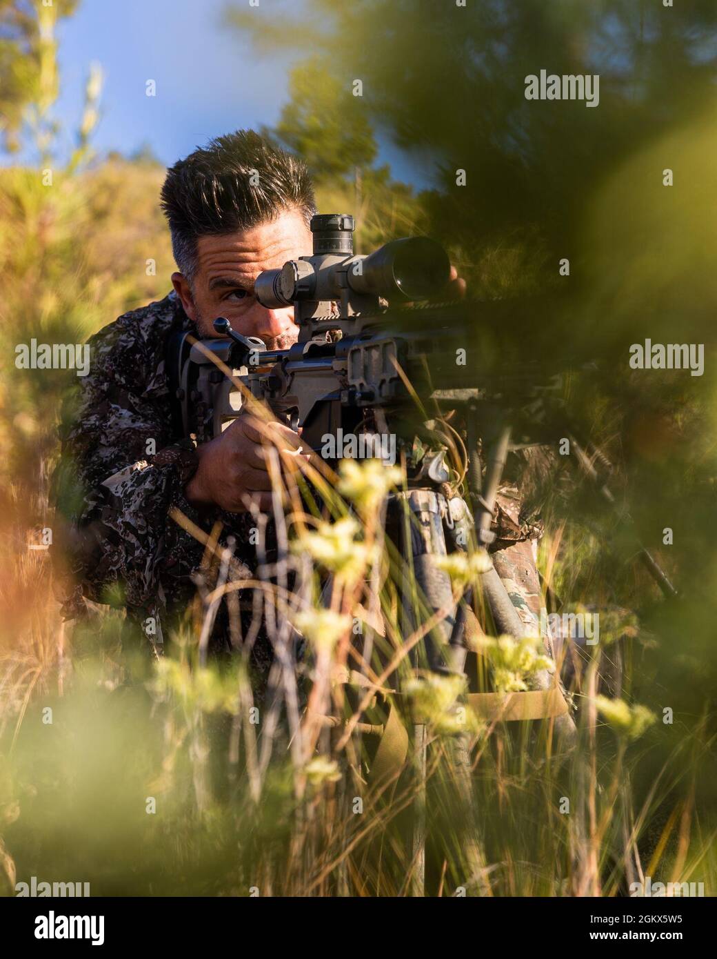 A Greek Special Forces Sniper instructor from the International Specialty Training Center (ISTC) surveys his surroundings at the ISTC Desert Sniper Course in Chinchilla, Spain on July 15, 2021. ISTC is a multinational education and training facility for tactical-level, advanced and specialized training of multinational special operations forces and similar units, employing the skills of multinational instructors and subject matter experts. Stock Photo