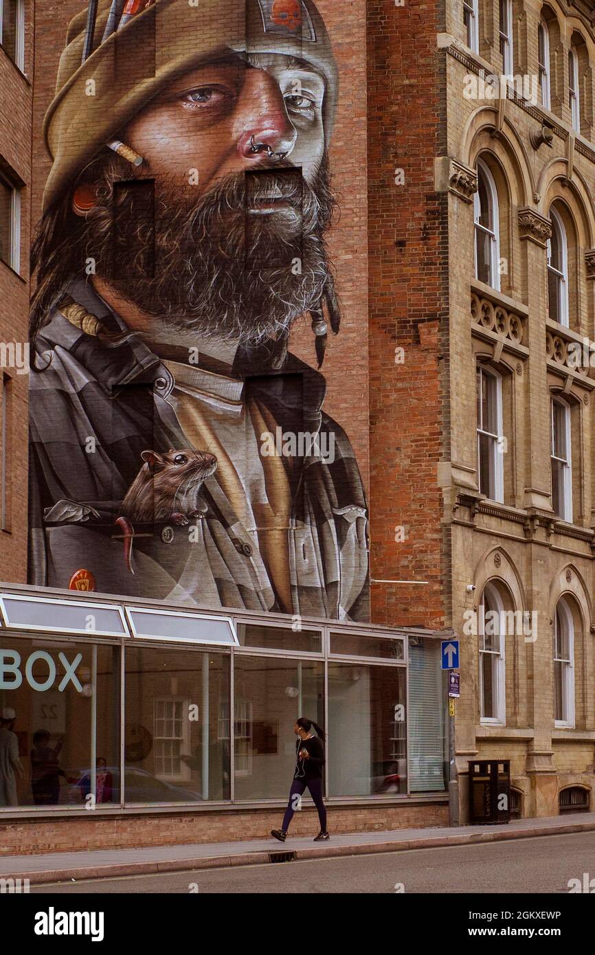 An amazing mural by the artist Smug on the wall of Leicester Creative Business Depot looms large above a passer by. Stock Photo