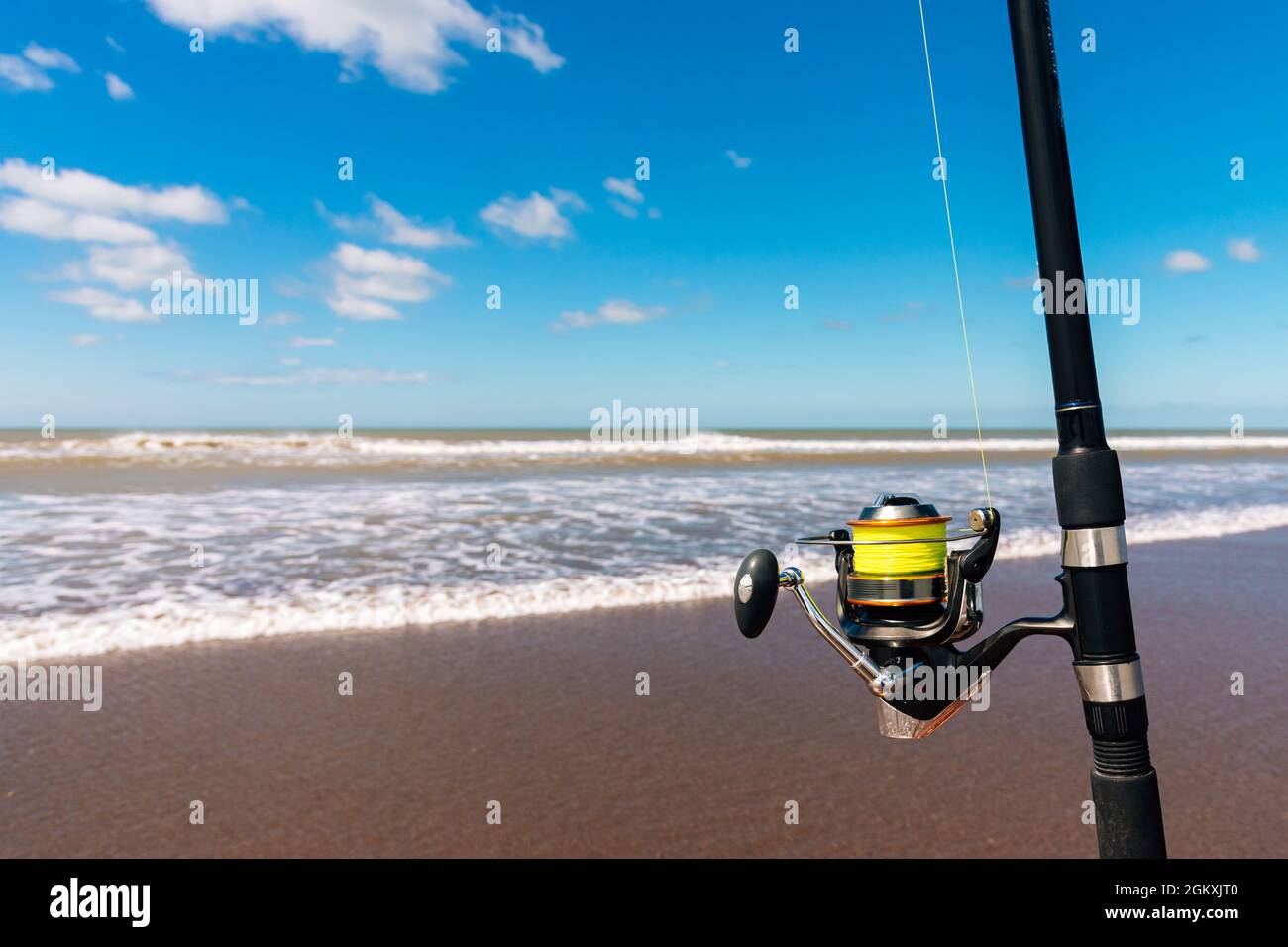 Close up of the fishing reel on his fishing rod on the beach on a beautiful sunny day. Horizontal photo. Stock Photo