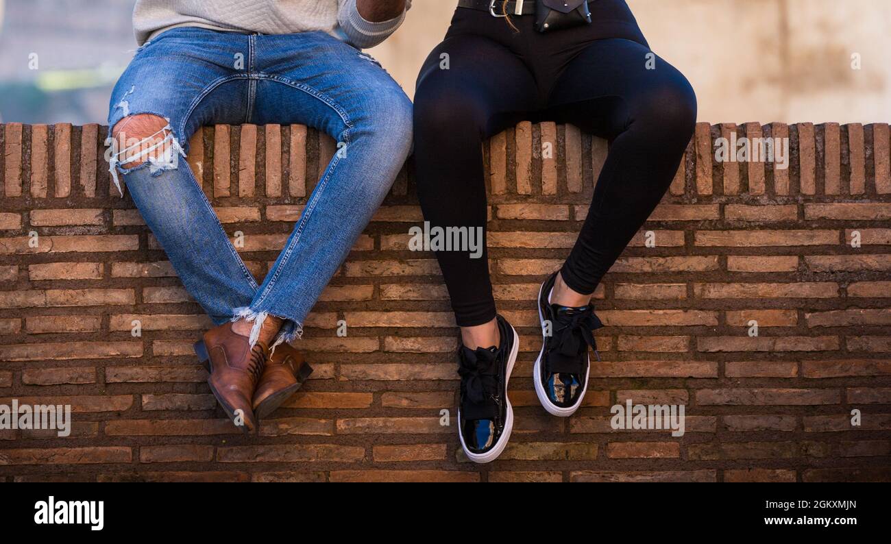 Couple sitting on brick roman wall undefined. Men in blue jeans and brown  boots, woman in black leggings and sneakers, orange wall as a bench Stock  Photo - Alamy