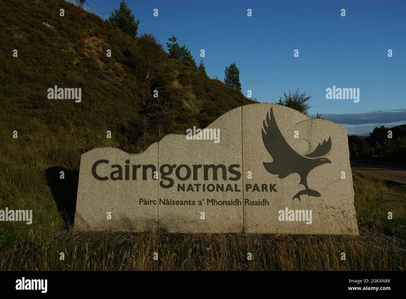Cairngorms National Park sign by side of A9 road. Lit by golden evening sun, blue sky and hill with greenery in background. No people. Stock Photo