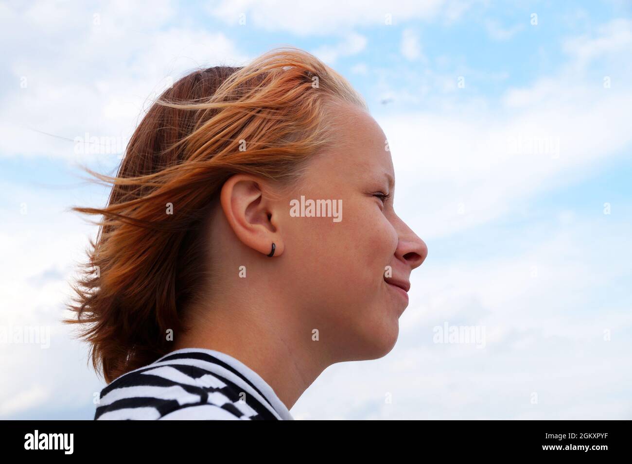 profile of smiling teenage girl with fluttering red hair against blue sky. Stock Photo