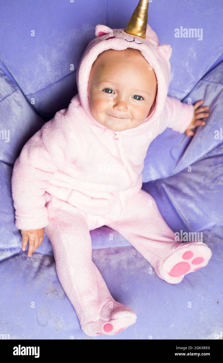 Baby in pink costume of unicorn. Kid is sitting alone on light