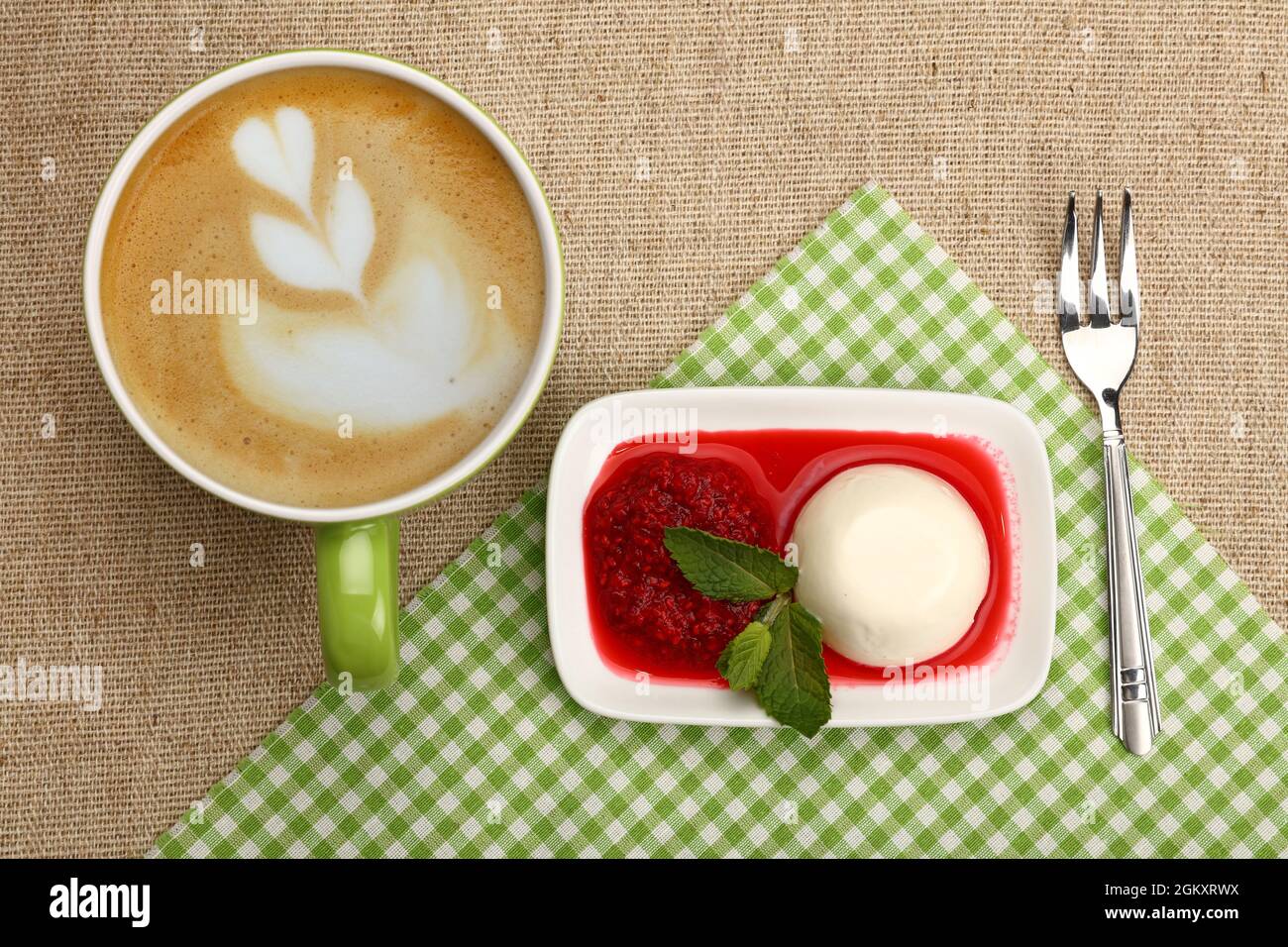 Close up serving panna cotta traditional Italian dessert with raspberry jam and cup of cappuccino coffee, elevated top view, directly above Stock Photo