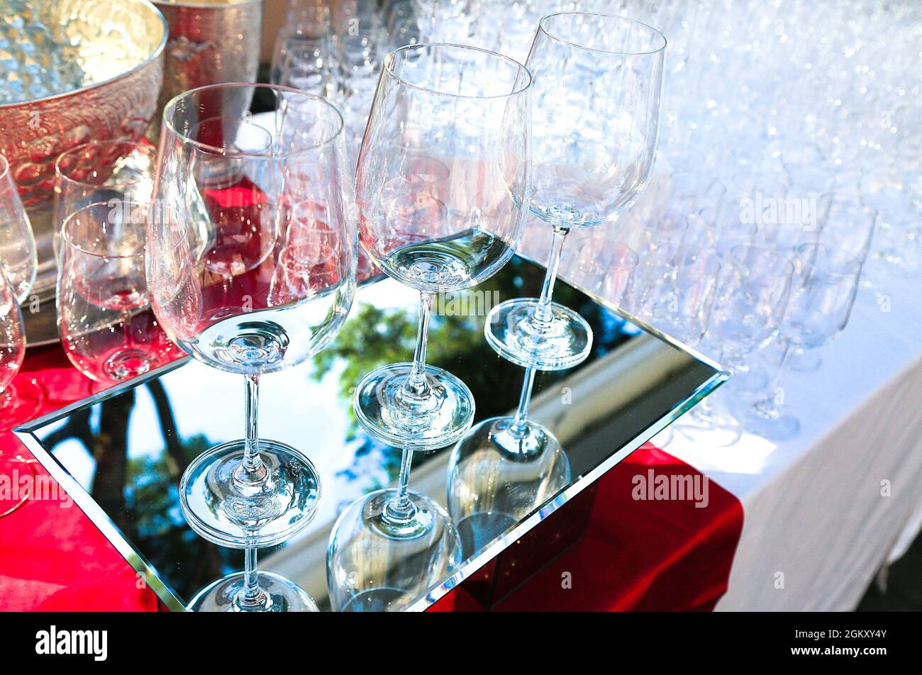 three crystal wine glasses on mirrored surface with many glasses behind. catering service. Wine tasting preparation. important party. Utensils for Stock Photo