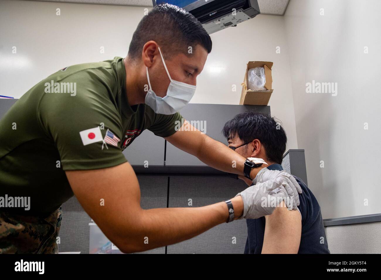 U.S. Navy Petty Officer 1st Class Javier Flores, a hospital corpsman with 3rd Medical Battalion, 3rd Marine Logistics Group, vaccinates a Master Labor Contractor aboard Marine Corps Installations Pacific, at the U.S. Naval Hospital Okinawa on Camp Foster, Okinawa, Japan, July 26, 2021. Vaccinating host-nation employees and military personnel will contribute to the prevention of further spread of COVID-19 in Japan and will protect the resilience of the alliance. Stock Photo