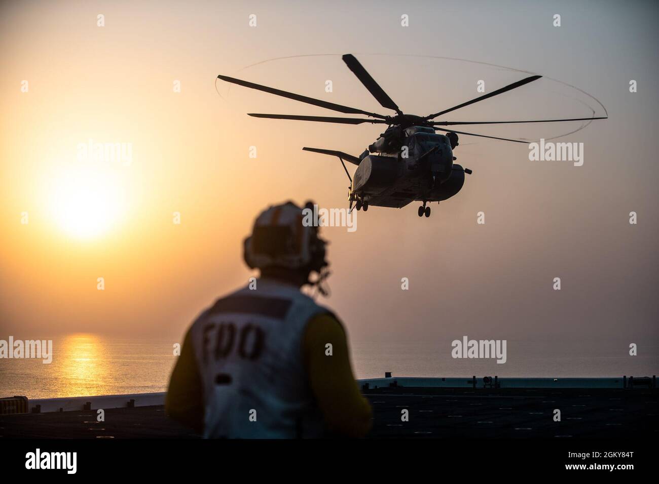 210726-N-N0146-1191 ARABIAN GULF (July 26, 2021) – Aviation Boatswain’s Mate (Handling) 1st Class Roy Brown assigned to expeditionary sea base USS Lewis B. Puller (ESB 3) observes an MH-53E Sea Dragon helicopter attached to Helicopter Mine Countermeasures Squadron (HM) 15 land on the flight deck during flight operations in the Arabian Gulf, July 26. Lewis B. Puller is deployed to the U.S. 5th Fleet area of operations in support of naval operations to ensure maritime stability and security in the Central Region, connecting the Mediterranean and Pacific through the western Indian Ocean and three Stock Photo