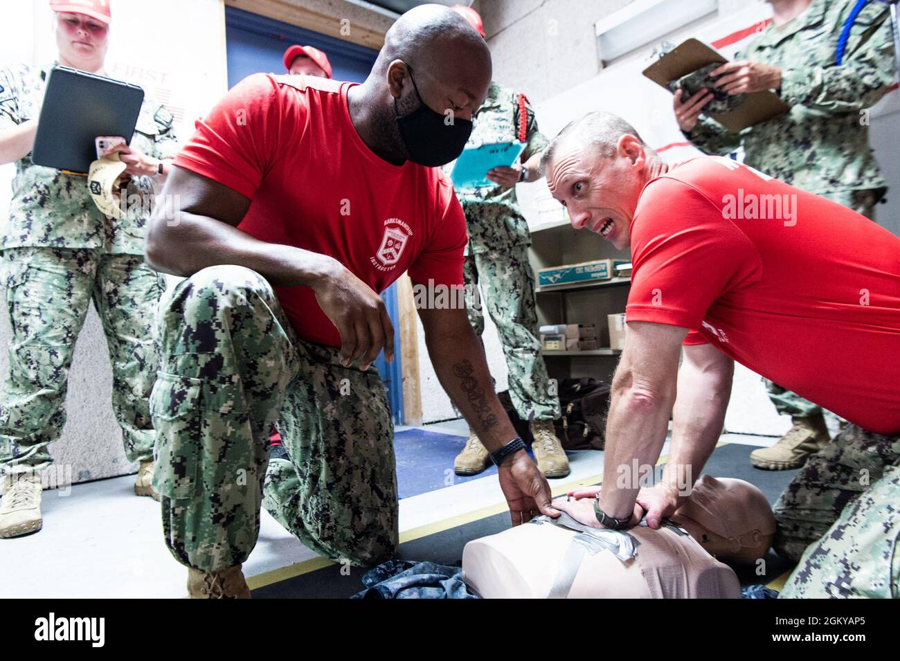 Chief Boatswain’s Mate Emeka Igwe and Chief Aviation Electronics Technician Chad Abel, both Recruit Division Commanders assigned to Officer Training Command Newport (OTCN), Rhode Island, dress a simulated sucking chest wound during an emergency action drill, July 27. High-risk training instructors are annually evaluated to maintain qualification to ensure a safe training environment. OTCN offers four officer training programs at Naval Station Newport, including Officer Candidate School, Officer Development School, the Limited Duty Officer and Chief Warrant Officer Academy, and the Naval Scienc Stock Photo