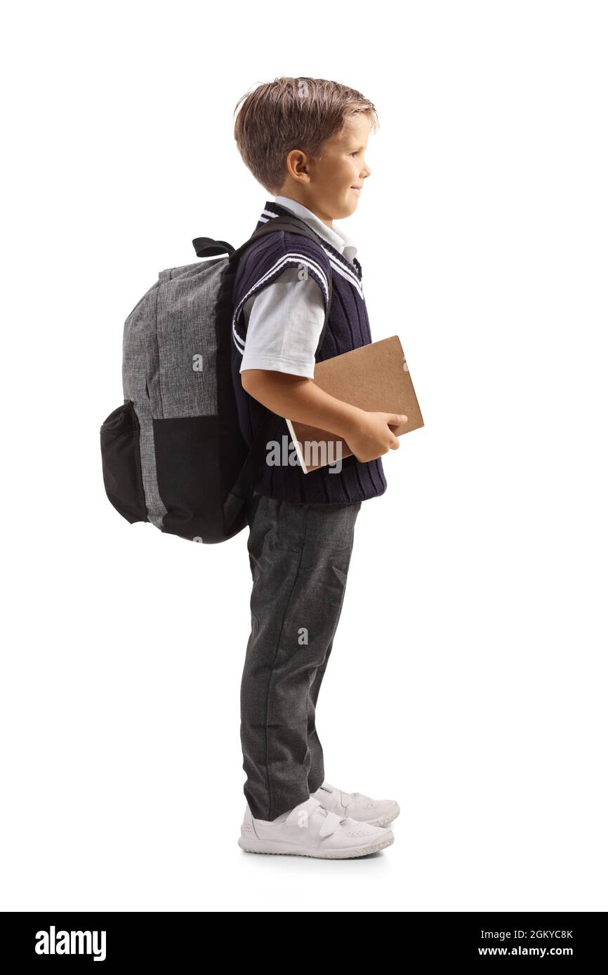 Full length profile shot of a schoolboy in a uniform standing and holding a book isolated on white background Stock Photo