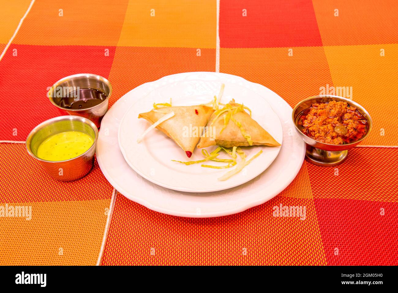 two vegetable samosas served in a Pakistani restaurant with sauces on an orange tablecloth Stock Photo