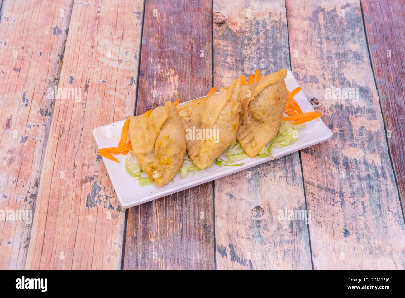 tray of fried samosas stuffed with lamb meat on a bed of iceberg lettuce and grated carrots on a wooden table Stock Photo