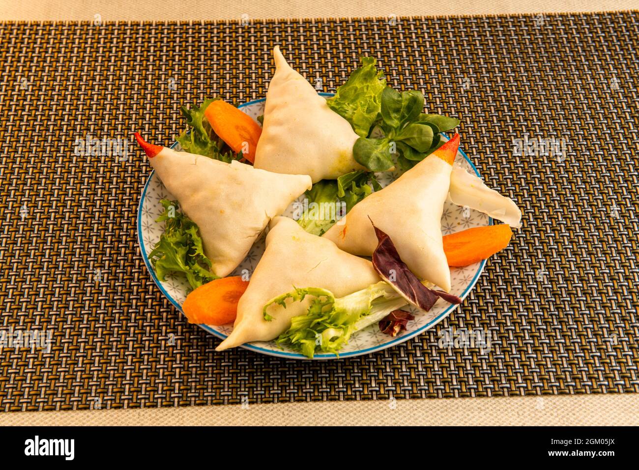 serving of Hindu vegetable samosa with lettuce and carrot garnish on a table in a Pakistani restaurant Stock Photo