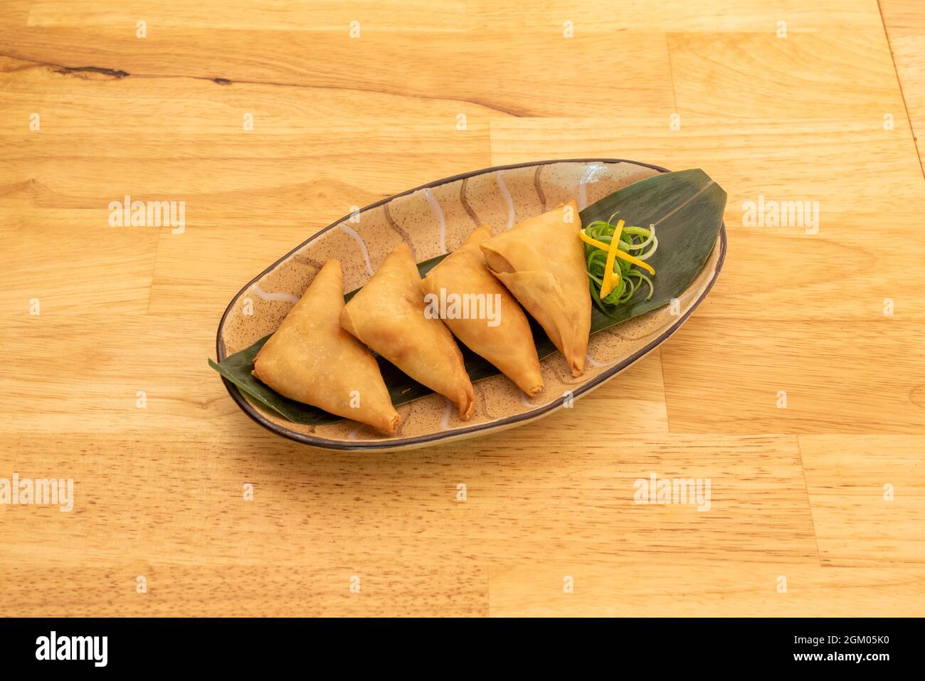 Tray of vegetable samosa cooked in Pakistani restaurant on banana leaf and oak table Stock Photo