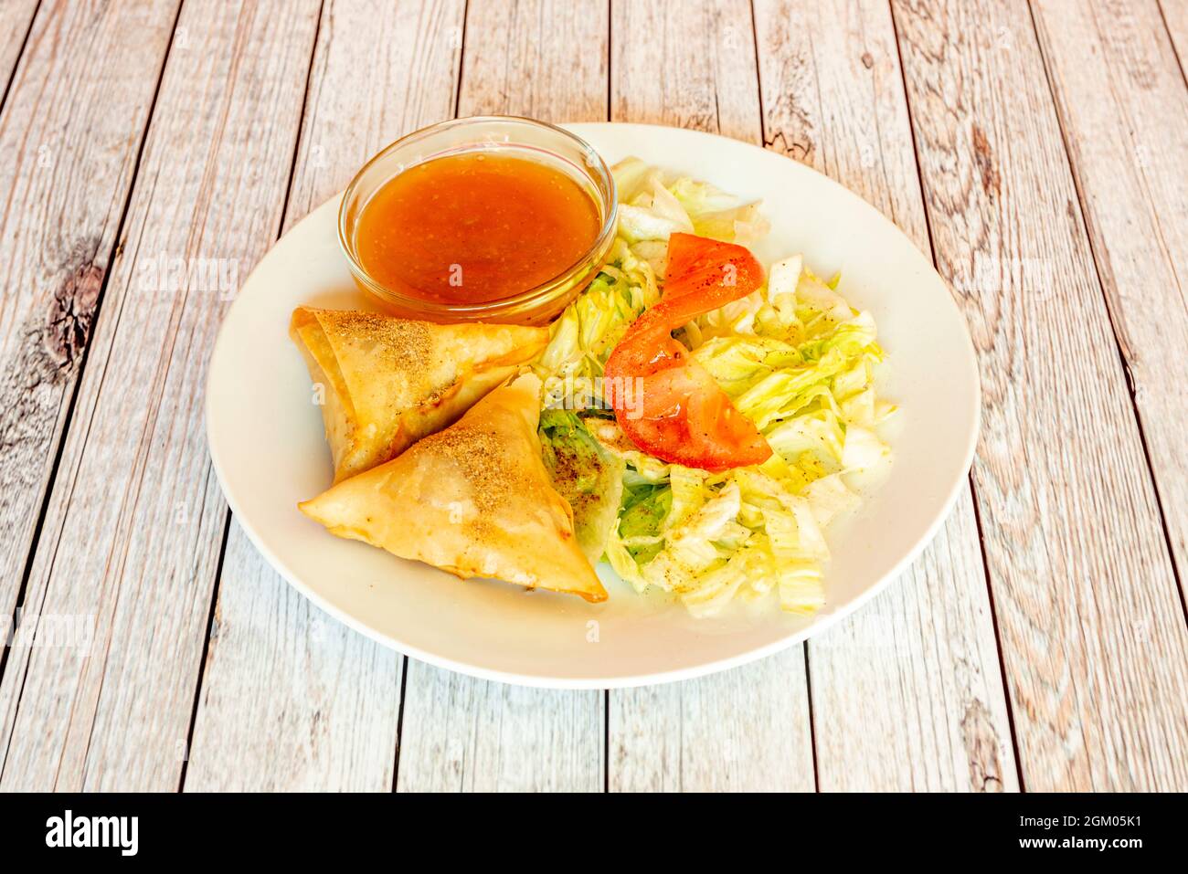 Vegetable samosa with spices, iceberg lettuce, tomato and dip sauce on white plate Stock Photo