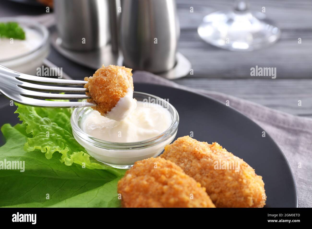 Dipping piece of salmon croquette into gravy boat with sauce on plate