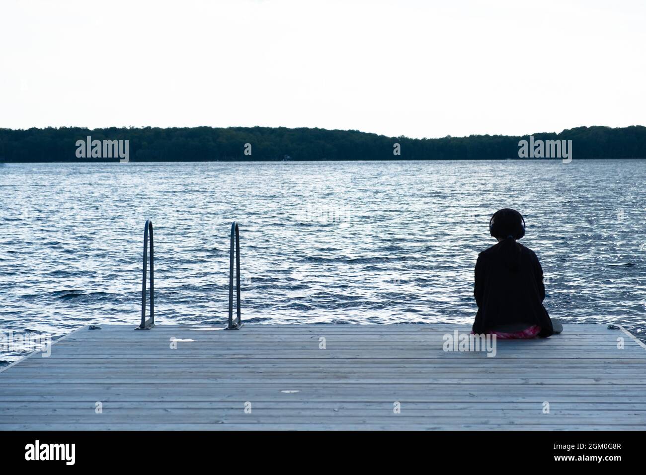 Girl looking out the water with her headphones on. Looking at her reminds me of my teenage years - confused with too much emotions I couldn't handle. Stock Photo