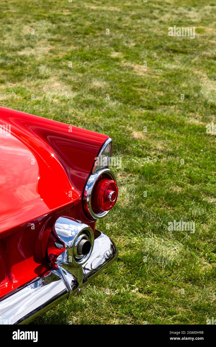 The right rear corner of a classic red 1955 Ford Thunderbird sports car showing the exhaust tailpipe through the bumperette. Stock Photo