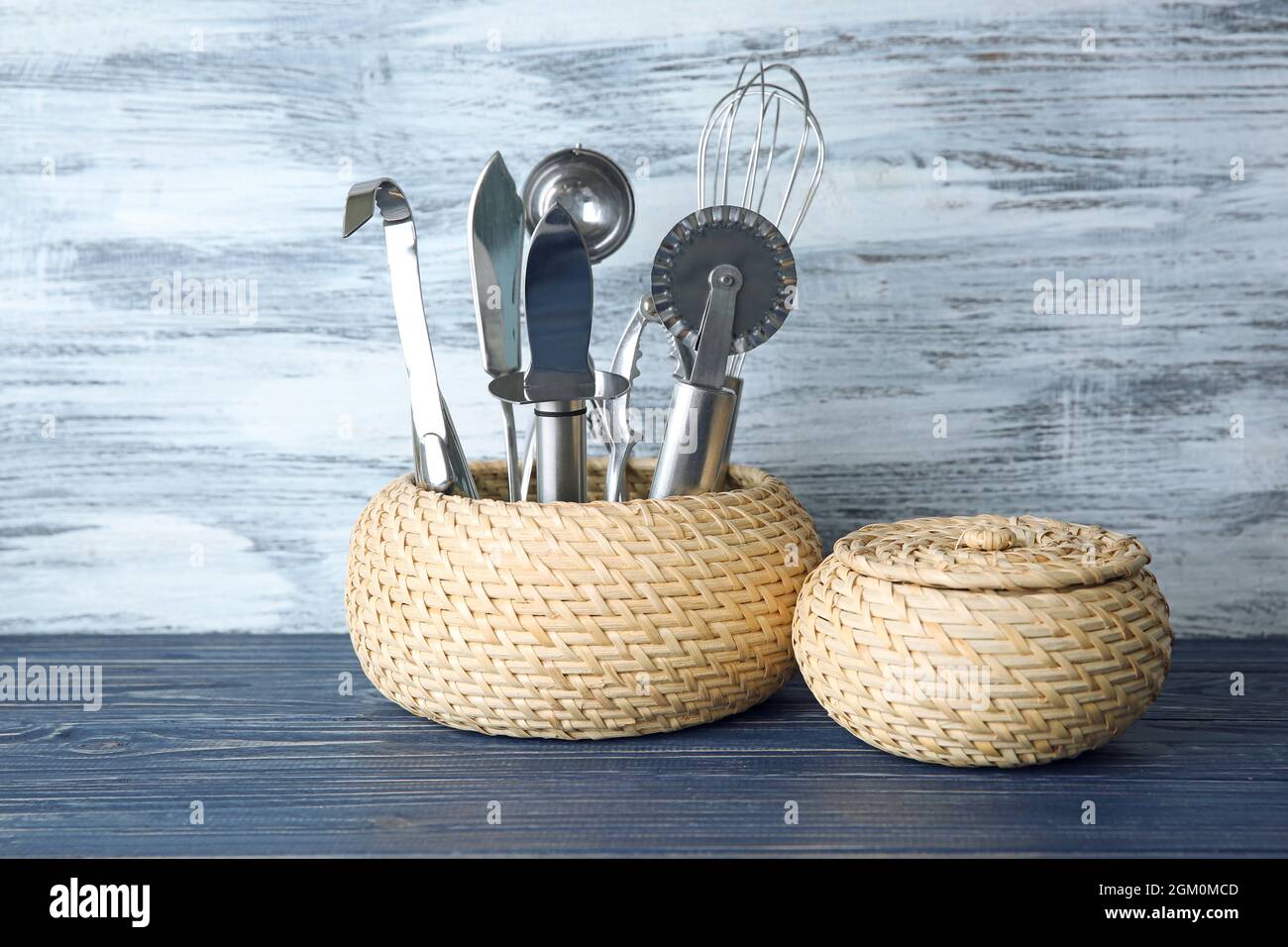 Kitchen utensils in wicker basket on table against wooden wall Stock