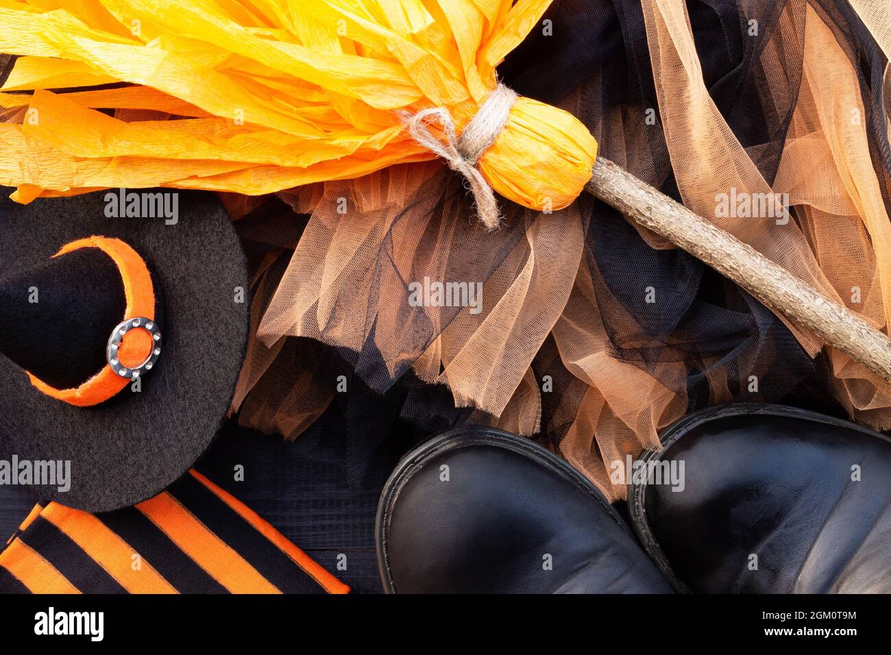 Orange and black Halloween flatlay. Witch clothes: stockings, boots, hat, broom, skirt on black background Stock Photo