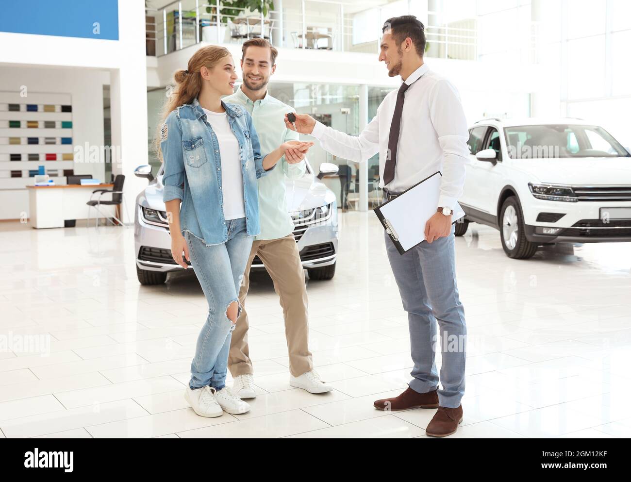 Car salesman giving key to couple in dealership Stock Photo - Alamy