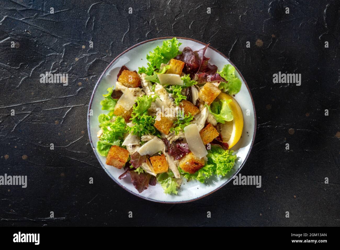 Chicken Caesar salad, overhead shot on a black background. Romaine leaves, crispy croutons and chicken fillet meat Stock Photo