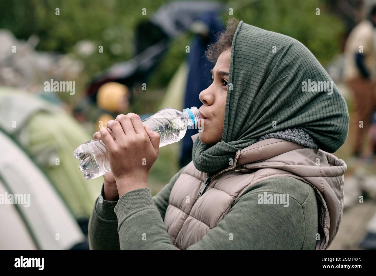 Teenage middle-eastern girl with scarf covering head drinking water greedily in refugee camp Stock Photo