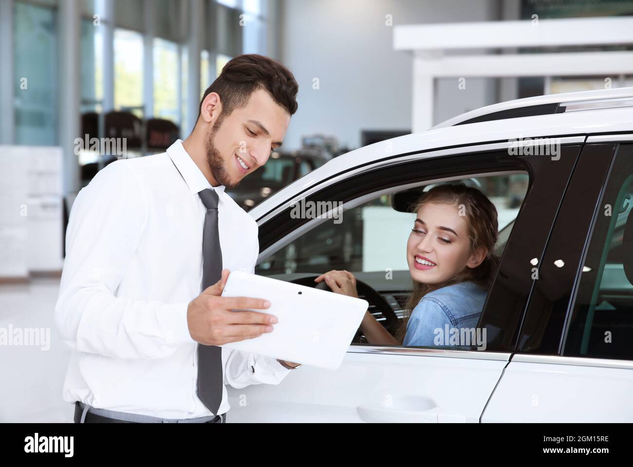 Woman sitting on driver's seat while talking to car salesman Stock