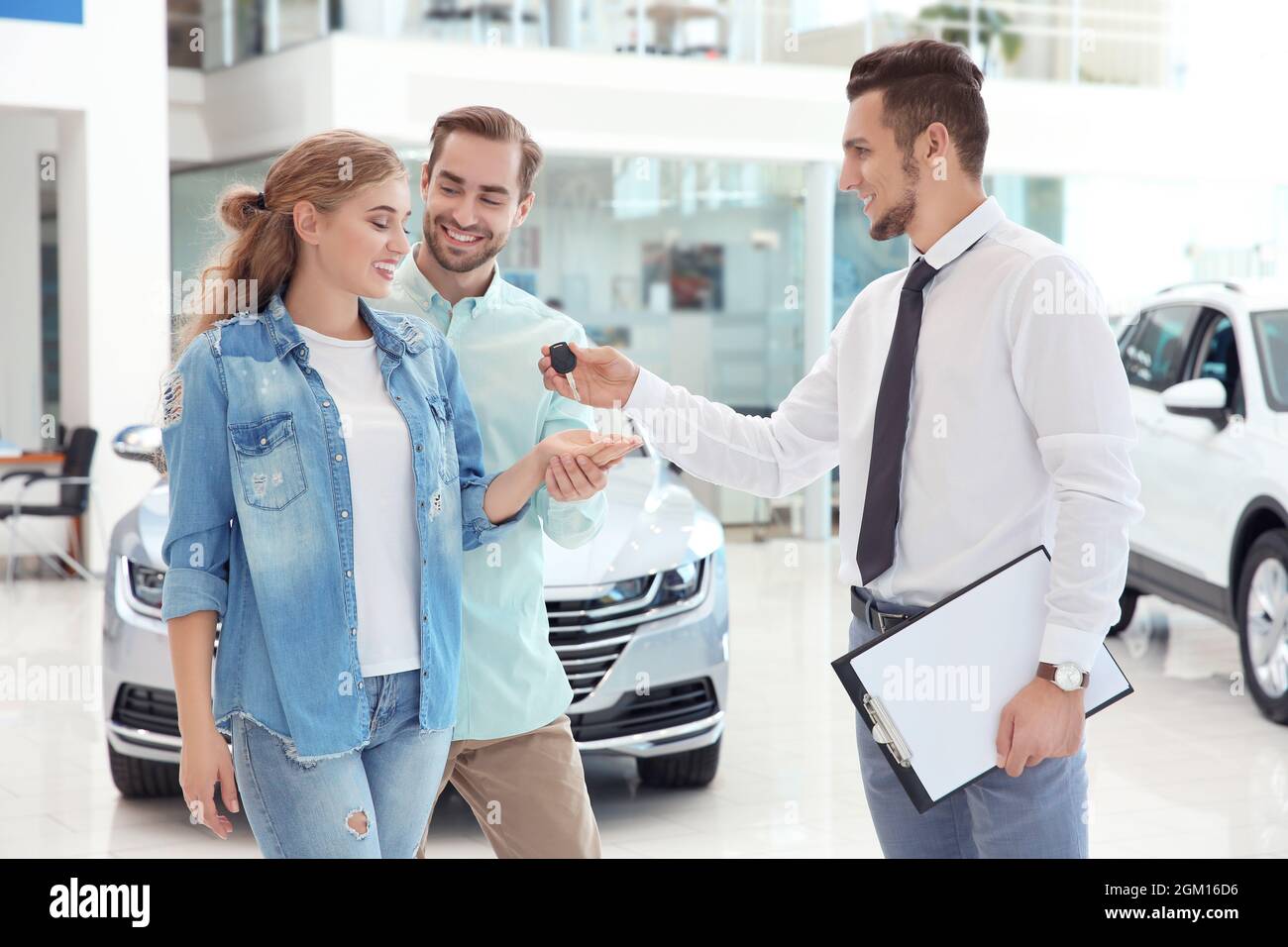Car salesman giving key to couple in dealership Stock Photo - Alamy