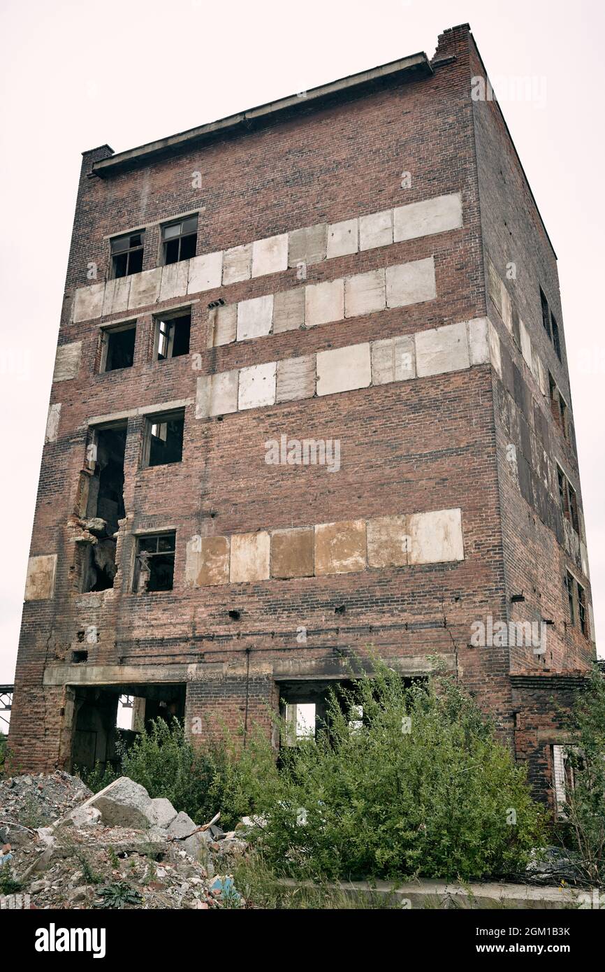 Gloomy abandoned brick building with broken windows and bushes, stones ...