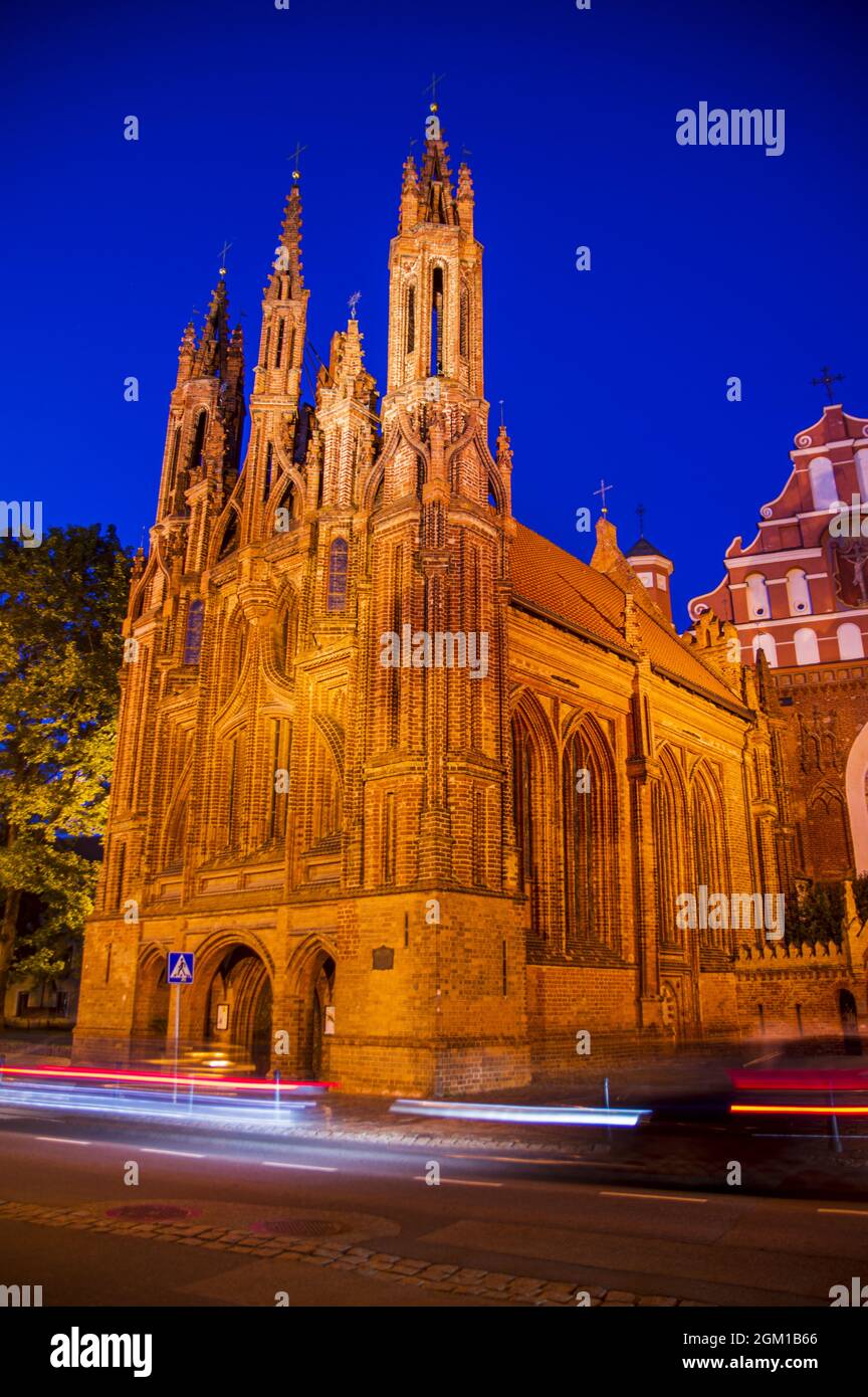 Illuminated beautiful old Orthodox Church in the old Town of Vilnius. Building with Gothic towers on The Main city street at night after sunset with the light trails. Car's motion blur Stock Photo