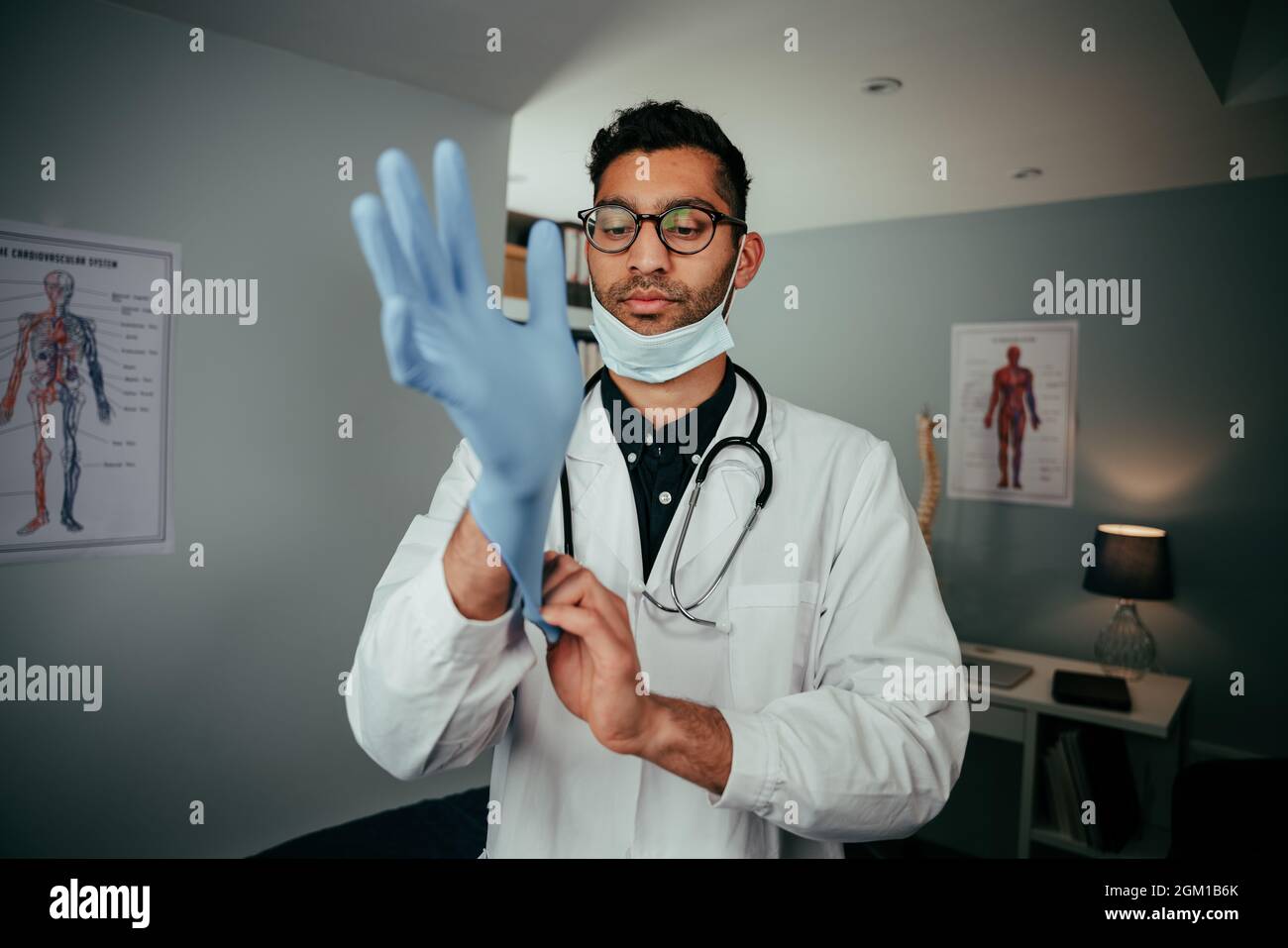 Mixed race male doctor standing in office wearing surgical gloves Stock Photo