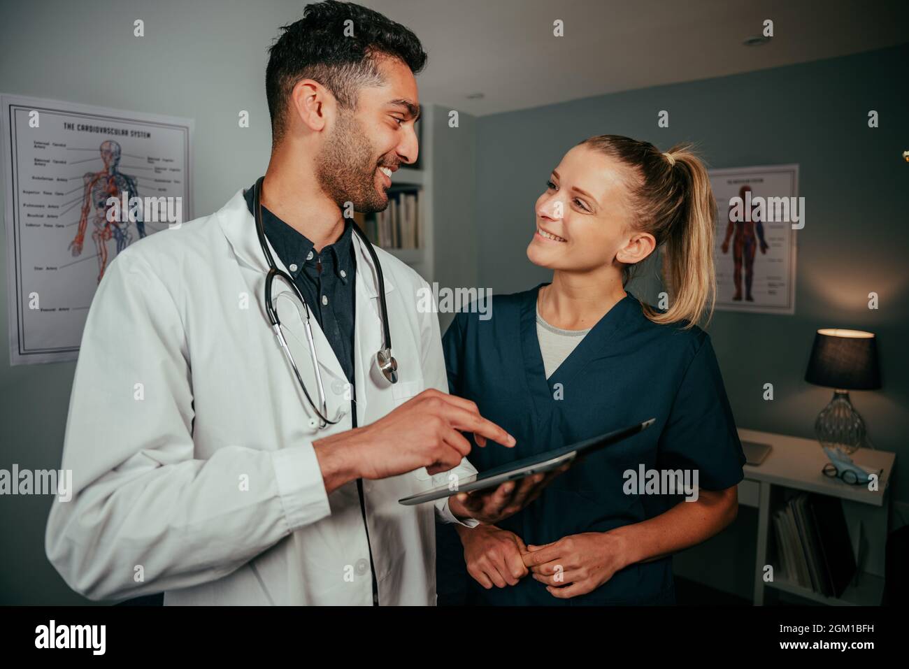 Mixed race male doctor and caucasian nurse chatting while discussing research on digital tablet Stock Photo