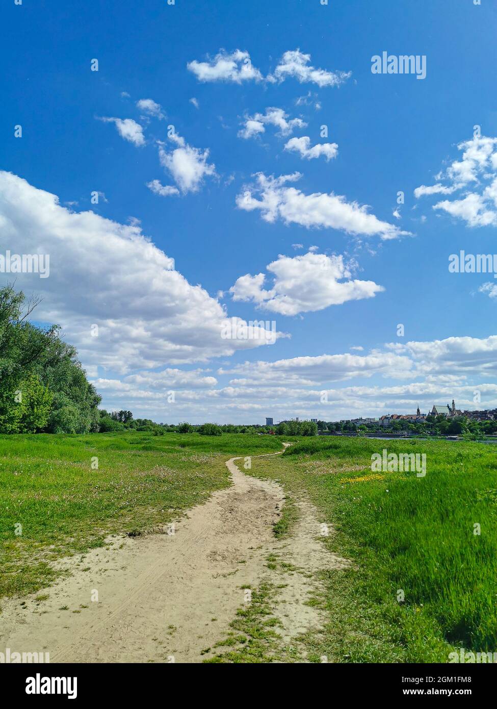 Beautiful view of the path in the park, green grass, blue sky with white clouds on a sunny warm day Stock Photo