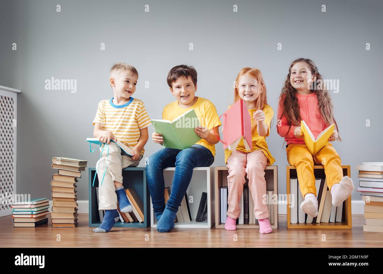 Group of children sitting on the book's stacks and on the bookshelves in the room and reading periodical. Stock Photo
