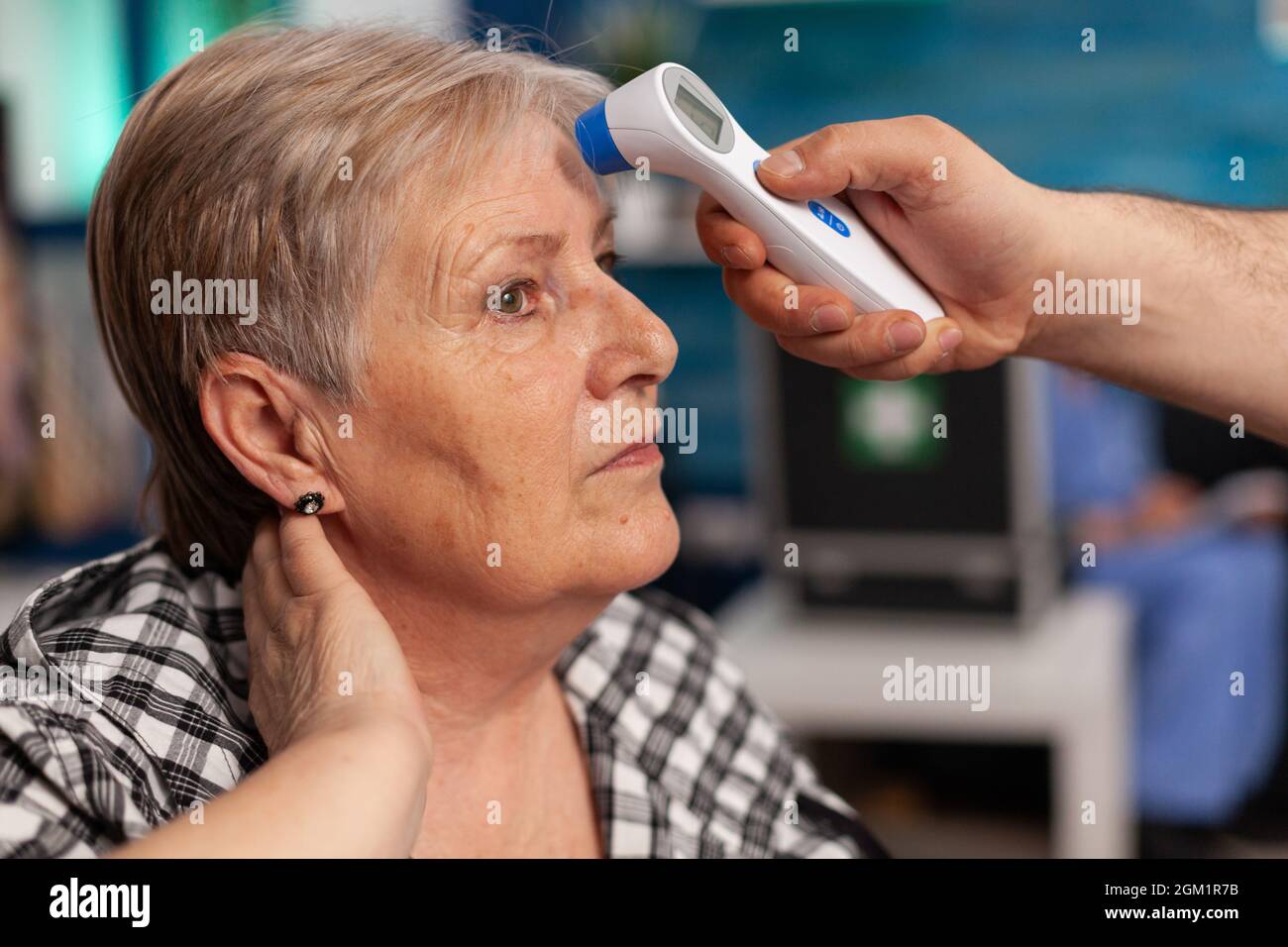 Close-up of assistant man helper checking temperature using medical infrared thermometer discussing with senior woman. Social services nursing elderly retired female. Healthcare assistance Stock Photo