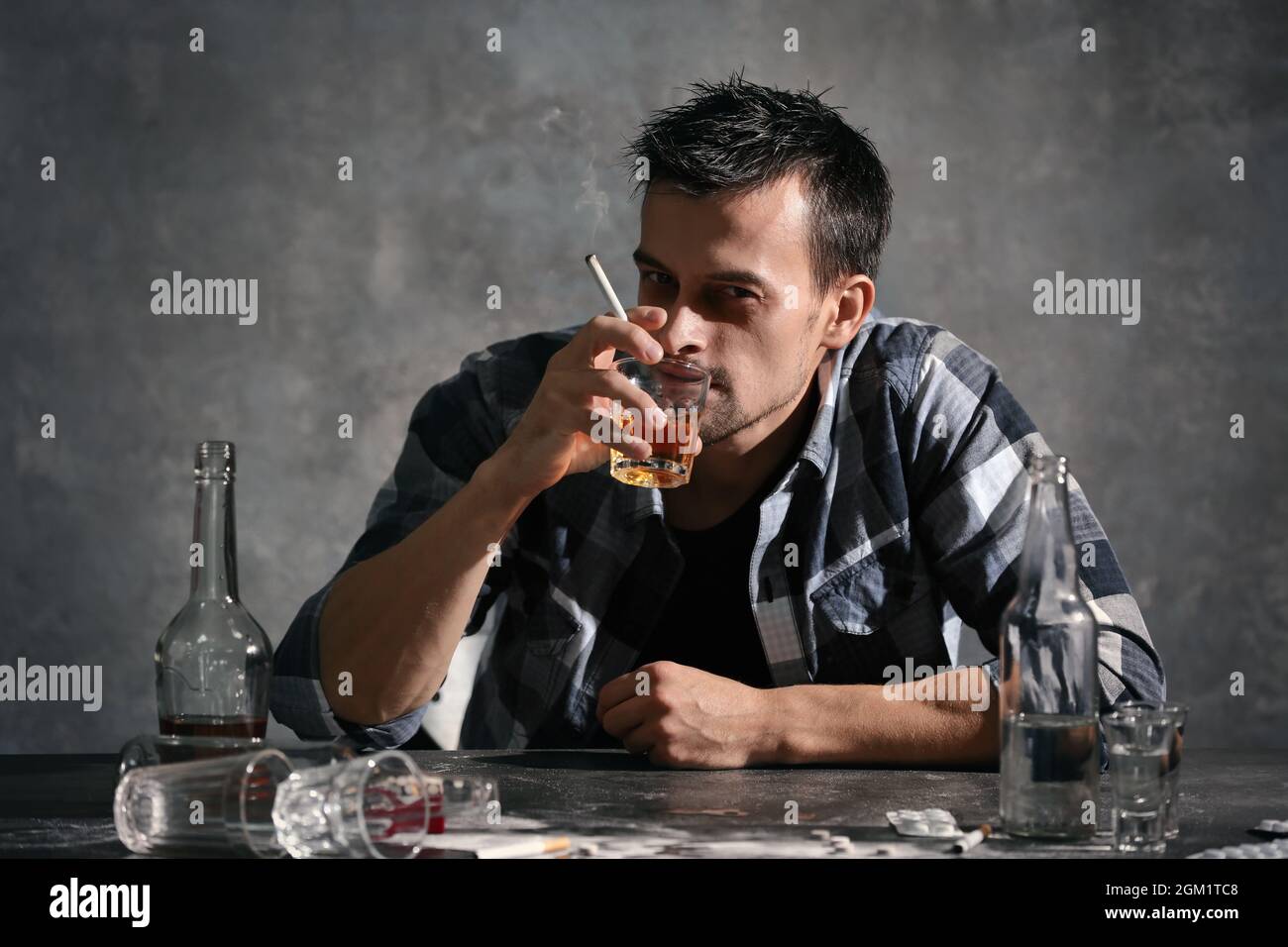 Man drinking alcohol and smoking cigarette while sitting at table Stock