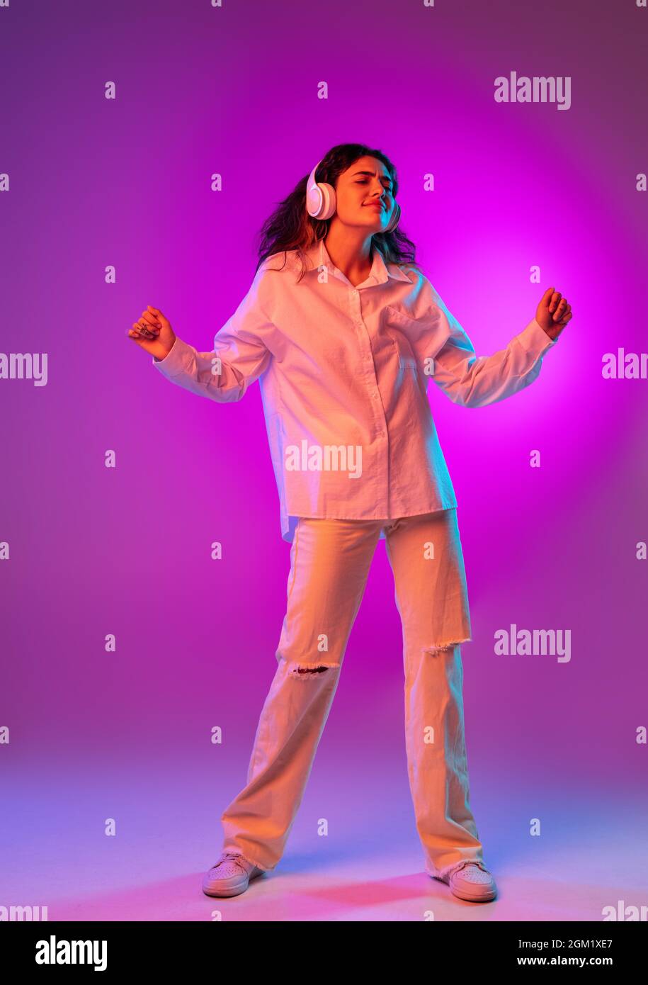 Portrait of Latino beautiful girl listening to music isolated on purple, lilac color studio background in neon light. Concept of human emotions Stock Photo