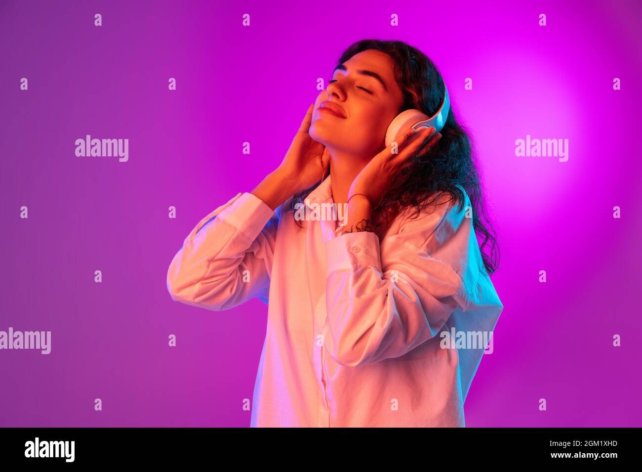 Portrait of Latino beautiful girl listening to music isolated on purple, lilac color studio background in neon light. Concept of human emotions Stock Photo