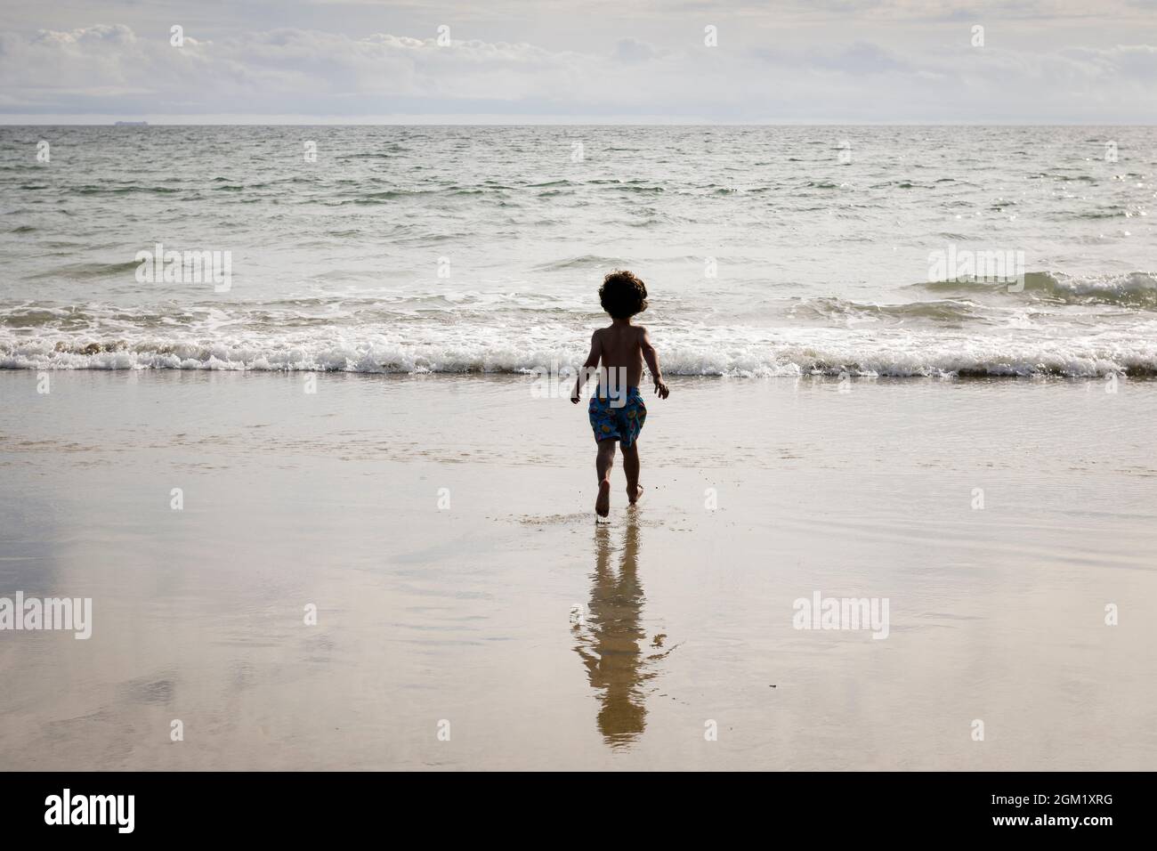 A child running towards the waters edge on Perranuthnoe Beach near Penzance, Cornwall. Stock Photo
