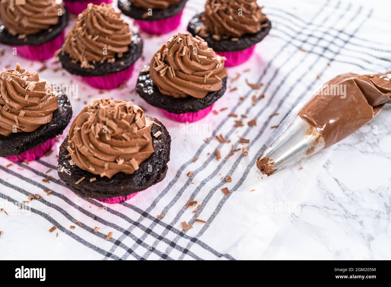 Piping chocolate ganache frosting on top of chocolate cupcakes Stock
